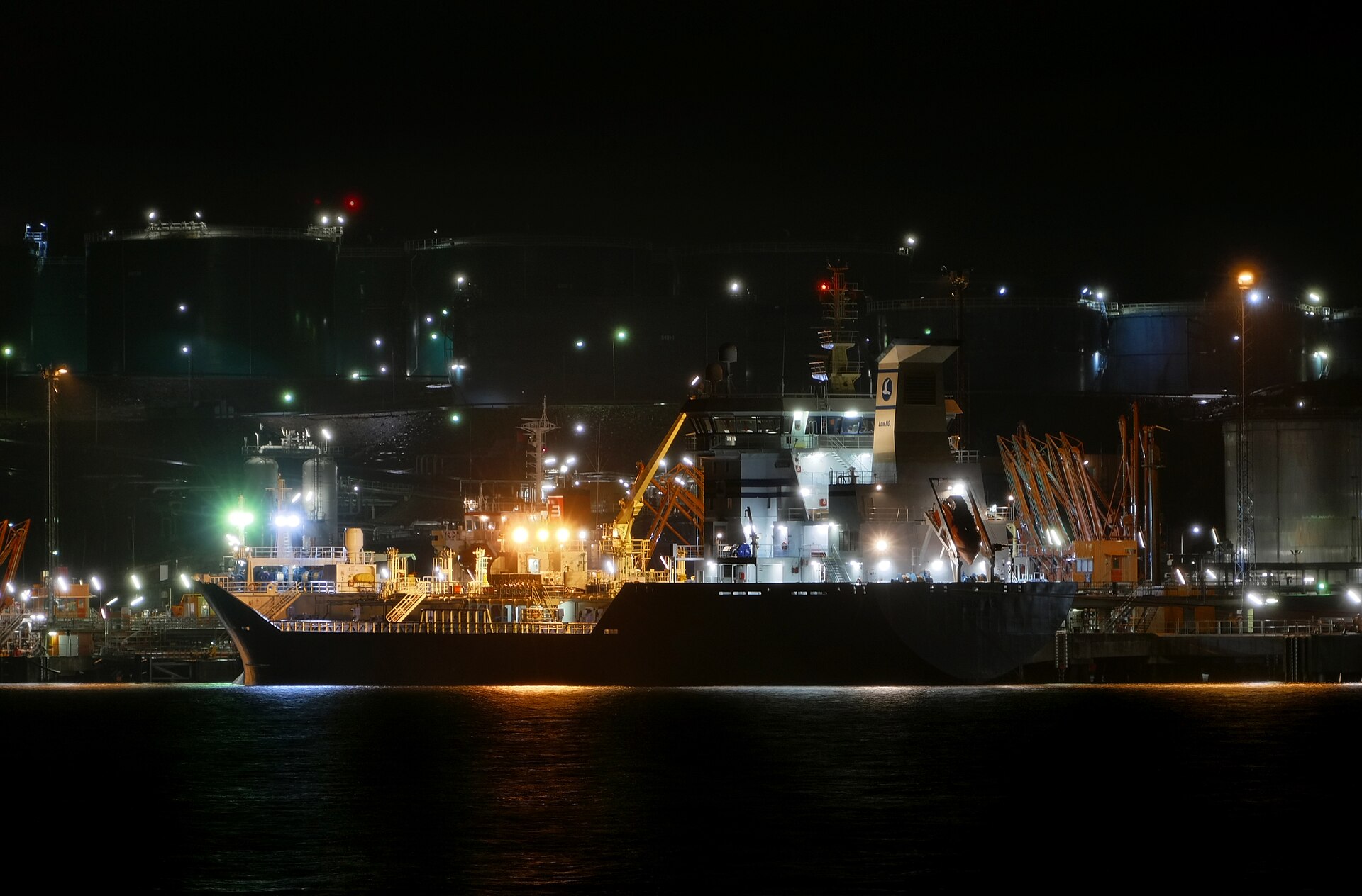 Navire-citerne à quai de nuit devant un terminal pétrolier éclairé
