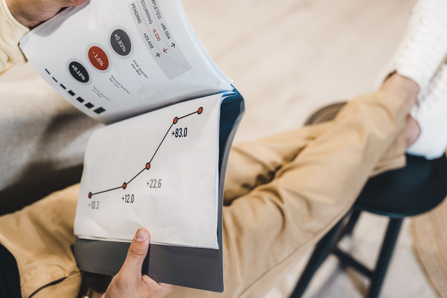 Personne assise tenant un rapport imprimé ouvert sur un graphique en courbe ascendante avec des valeurs chiffrées, vue de dessus.